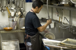 Hispanic male worker washing the dishes at a restaurant kitchen